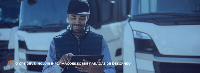 Caminhoneiro sorrindo e mexendo em um tablet com caminhões atrás.